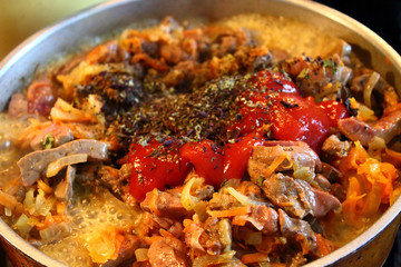 Liver and vegetables are fried in a frying pan on the stove. Close-up. Background.