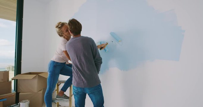 Cute couple painting wall in new home and kissing, happy new homeowners, home painting