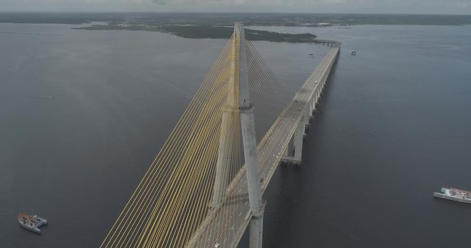 Aerial descending beside the cable-stayed Rio Negro Bridge that links the cities of Manaus and Iranduba in the Brazilian Amazon with water on either side as a traffic crosses from one side to another