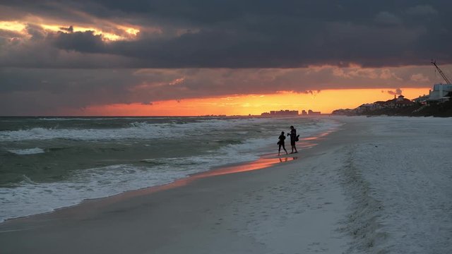 Couple people silhouette looking at dramatic orange red sunset in Santa Rosa Beach, Florida with Pensacola coastline coast in panhandle with ocean gulf mexico waves