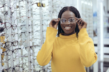 Young pretty african woman choosing prescription glasses frames in Optician's shop.