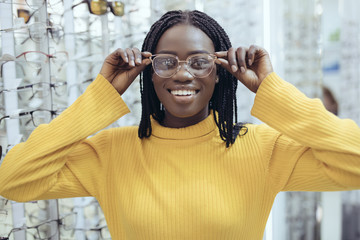 Young pretty african woman choosing prescription glasses frames in Optician's shop.