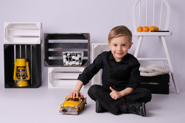 A white, blond haired boy, dressed in black in the studio on a white background. A modern, minimalist style with white, black and yellow color. Whole body, sitting.