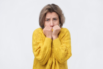 Shocked european woman in yellow sweater biting her fist in fear