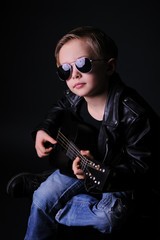 Obraz na płótnie Canvas A boy dressed in black with dark glasses, playing the guitar. Clouse up, black background, studio shot.