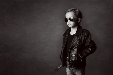 Boy, 5 years old, dressed in black, stylish, sunglasses, on a dark background in the studio, Looking side with Copy Space. Little handsome.