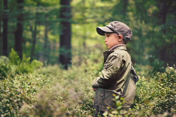 A boy in the forest, standing among trees, stands sideways. He is dressed in a green jacket and hat, wandering, looking for something or lost his way. cover photo of the book.