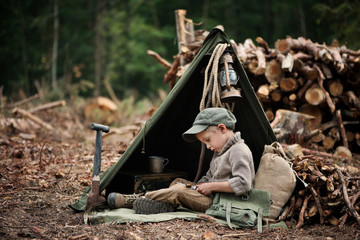 The boy, 5 years old, looks like a trapper, wanderer, lumberjack. Hut, shelter in the forest among...