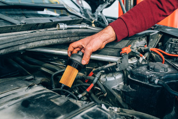 Auto mechanic working in garage during the maintenance of engine. Mechanician holding oil filter...