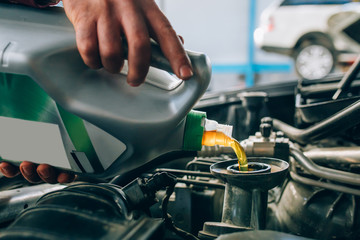 Auto mechanic working in garage during the maintenance of engine. Mechanician pouring fresh oil...