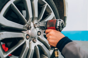 Mechanician changing car wheel in auto repair shop. Mechanic adjusting the tire wheel by using hand and tool at the repair car garage