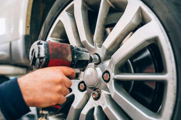 Mechanician changing car wheel in auto repair shop. Mechanic adjusting the tire wheel by using hand...