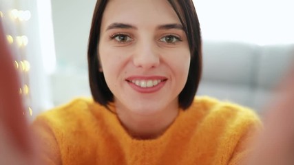 Happy woman broadcasts online video chat talking with her friend holding smartphone at home blowing kiss