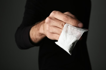 Drug dealer holding bag with cocaine on dark background, closeup