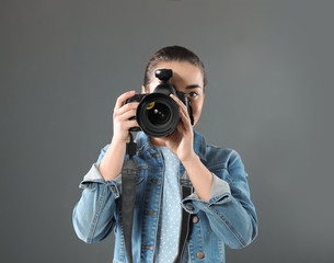 Young woman with camera against gray background. Professional photo studio