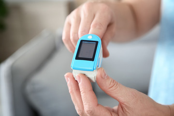Mature woman checking pulse with medical device at home, closeup