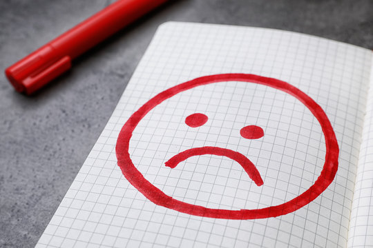 Notebook with drawing of unhappy face on table, closeup. Depression symptoms
