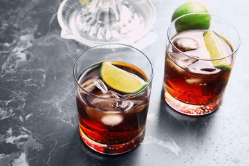 Glasses of cocktail with cola, ice and cut lime on marble background