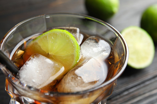 Glass of cocktail with cola, ice and cut lime on table, closeup