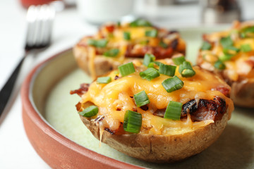 Plate of baked potatoes with cheese and bacon on table, closeup