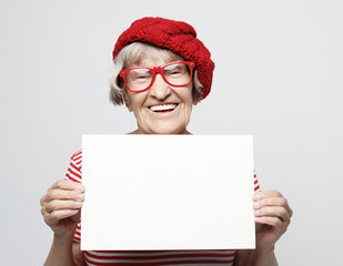 Portrait of happy senior woman with blank advertising board or copy space, over light grey background