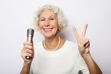 Portrait of charming modern grandmother holds up the microphone stand and sings  