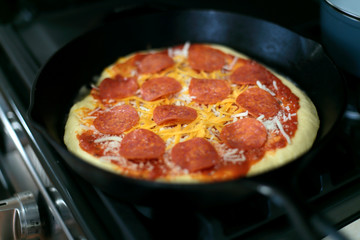Pepperoni pizza prepared on a cast iron pan about to be put in the oven to bake.

