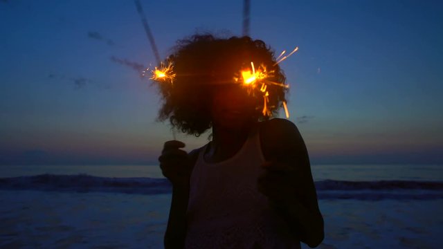 Silhouette of ethnic girl enjoying Thanksgiving party with sparklers on beach