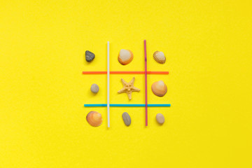 Fototapeta premium Tic-tac-toe. Choice Competition Game Between seashell and sea stone on yellow background. Sea style. Minimal concept. 