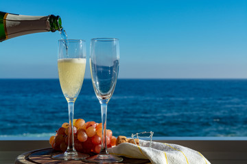 Waiter pouring Champagne, prosecco or cava in two glasses on outside terrace with sea view