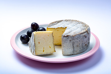 Round mature French Tomme cheese with one cutted piece close up isolated