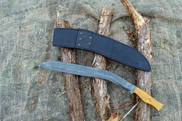 An extra large traditional style Kukri knife and leather sheath on top of cedar branches and burlap.