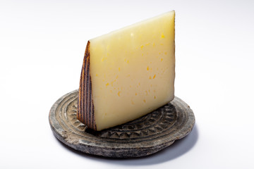 Piece of Spanish hard scheep milk cheese Manchego on grey stone plate isolated close up