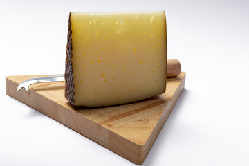 Piece of Spanish hard scheep milk cheese Manchego on wooden cheese plank isolated close up