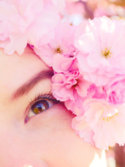 Woman`s eye and flower. Relaxed beautiful face of a young girl with clear skin and pink flowers. Beauty treatment concept. Good vision. Sakura blooming.