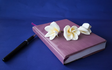 Pencil and flowers on a notebook on a blue background