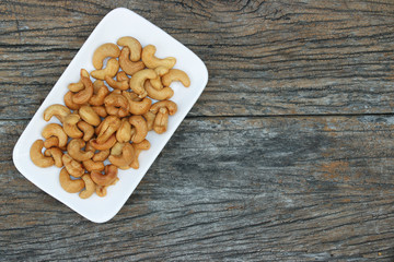 Tasty cashew nuts in white square dish on wooden table background with copy space, top view..