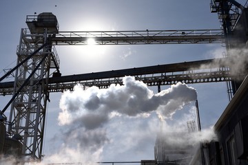 Low angle view of a factory with metal tower, bridges, and a smoke stack exhaust cloud