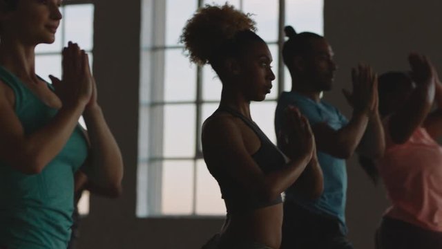 yoga class of young multiracial people practicing warrior pose enjoying healthy lifestyle exercising early in fitness studio meditation at sunrise
