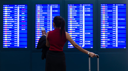 business woman in international airport looking at the flight information board, holding passport in her hand, checking her flight:business
