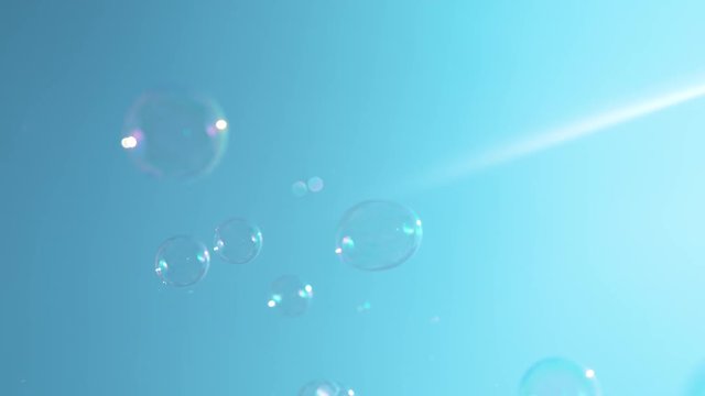 SLOW MOTION, MACRO, DOF: Bright summer sun ray shines onto the colorful soap bubbles flying around the sunny nature. Beautiful slow motion shot of small bubbles floating towards the clear blue sky.