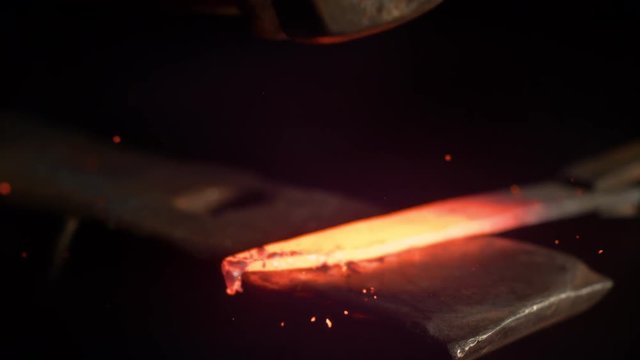 SUPER SLOW MOTION, MACRO, DOF: Metalworker forging a hot piece of metal into a beautiful knife blade. Cinematic shot of a glowing blade getting struck by a large hammer. Craftsman manufacturing blade.