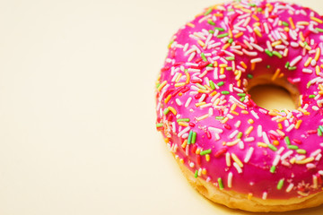 Bright donut in a pink glaze with a multi-colored rainbow sprinkle on a yellow background. 