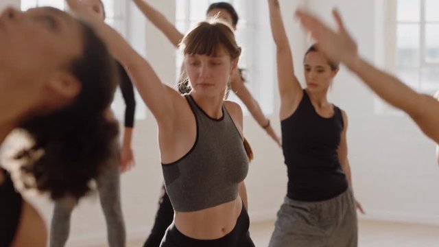 beautiful caucasian yoga woman practicing triangle pose meditation with group of multiracial women enjoying healthy lifestyle exercising in fitness studio at sunrise