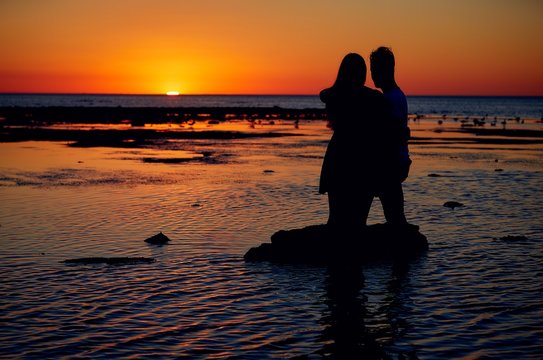 A Couple Look Out To Sea At Sunset