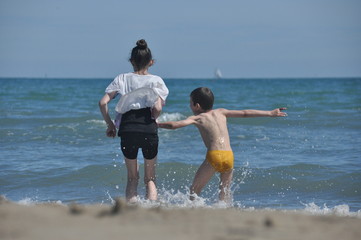 Children, siblings playing on the sea shore. They jumping in the waves.