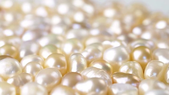 White and gold pearls rotating on white background surface. Close up 4k footage.