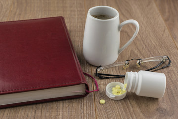 overcoming sleepiness: Tablets of ephedrine, coffee, glasses and book on a wooden table