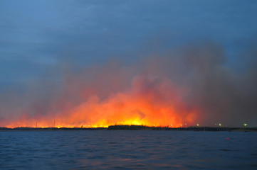 A large fire in a field near the water