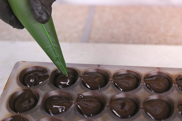 Baker's hands pouring liquid chocolate filling praline in form from pastry bag.